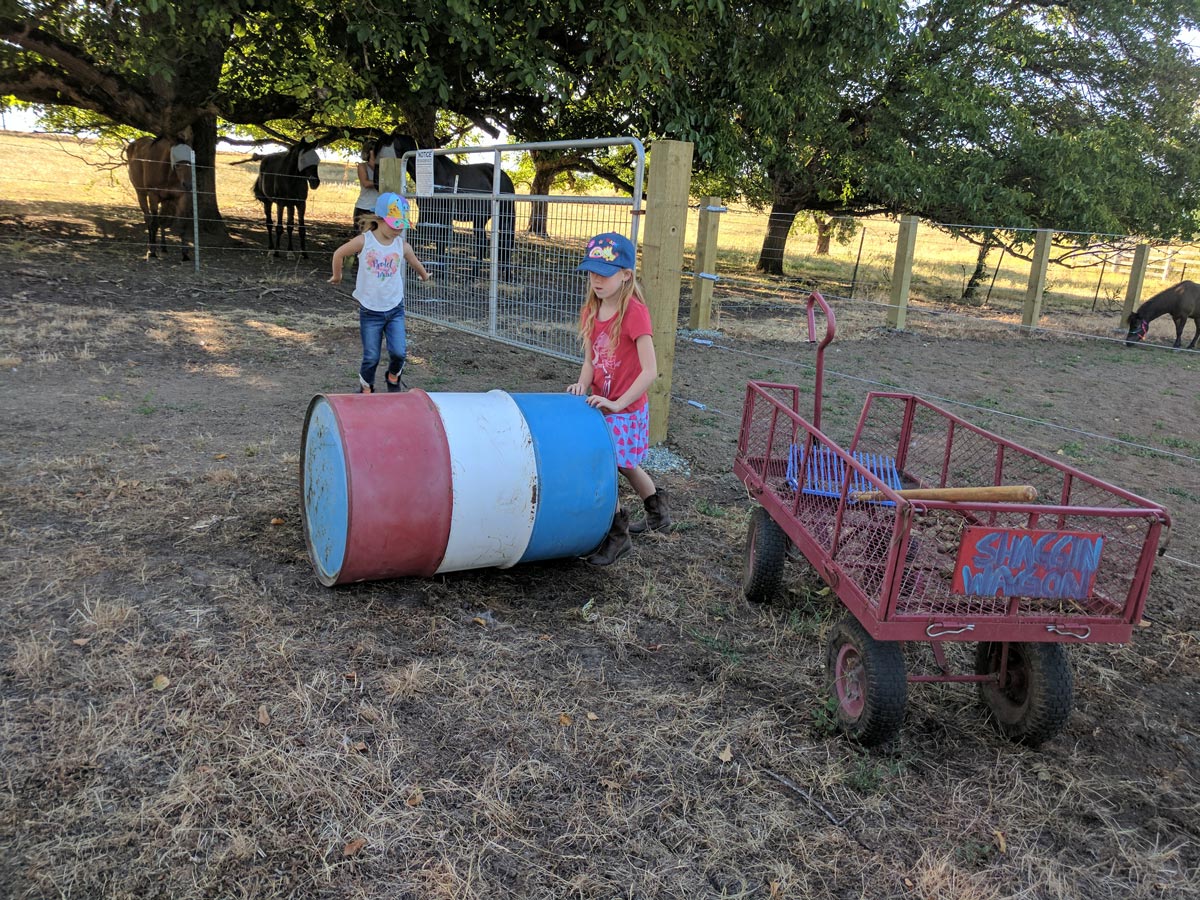Two young girls play near a colored barrel next to the arena fence